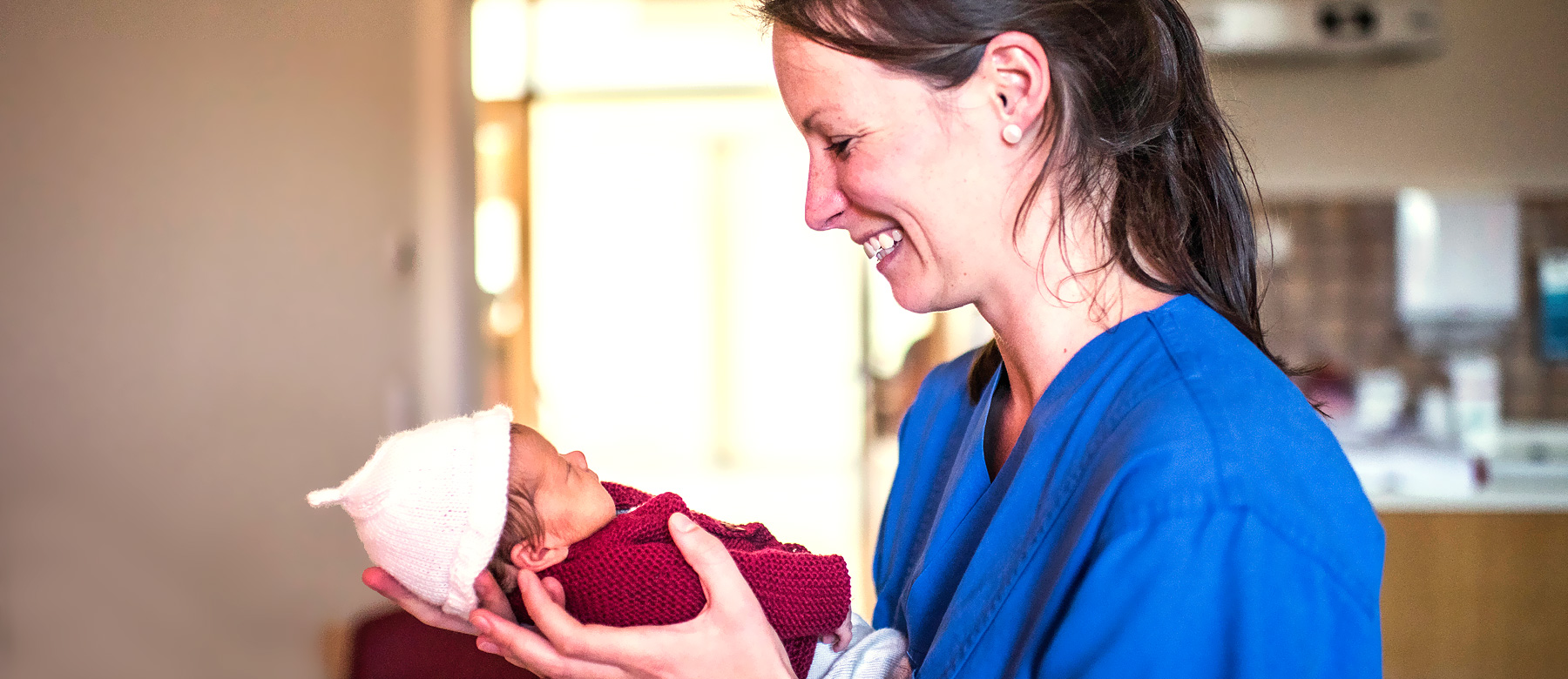 Kinderkrankenpflegerin hält ein frühgeborenes Baby in den Händen und lächelt.